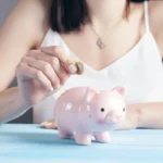 Hand dropping a coin into a pink polka-dot piggy bank