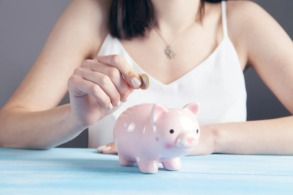 Hand dropping a coin into a pink polka-dot piggy bank