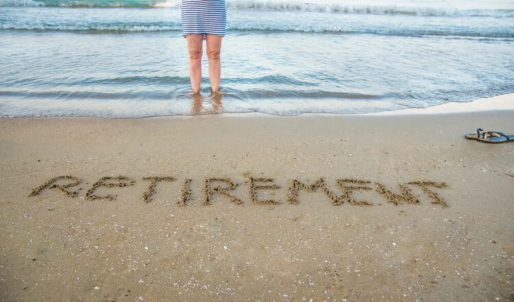 Retirement written in beach sand with figure at water's edge