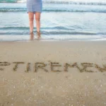 Retirement written in beach sand with figure at water's edge