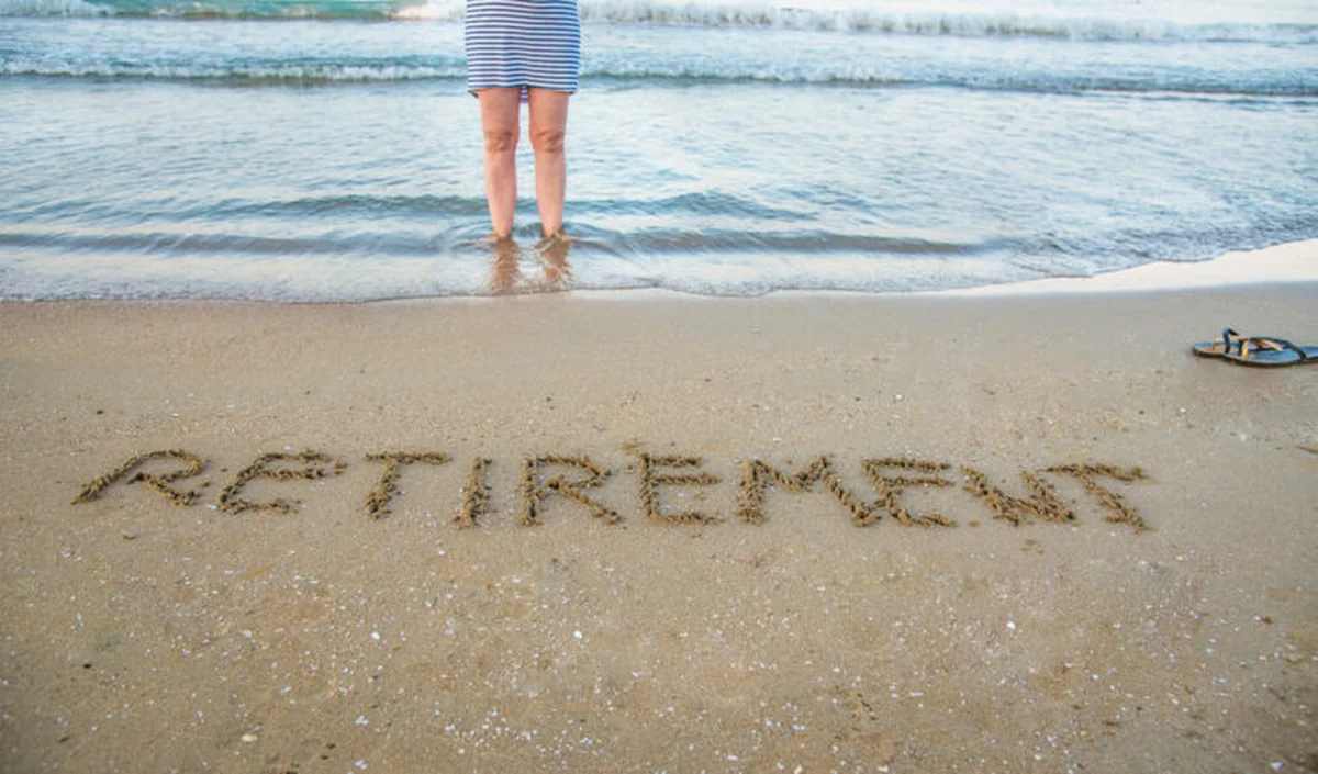 Retirement written in beach sand with figure at water's edge