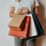 Person holding four shopping bags against a plain wall