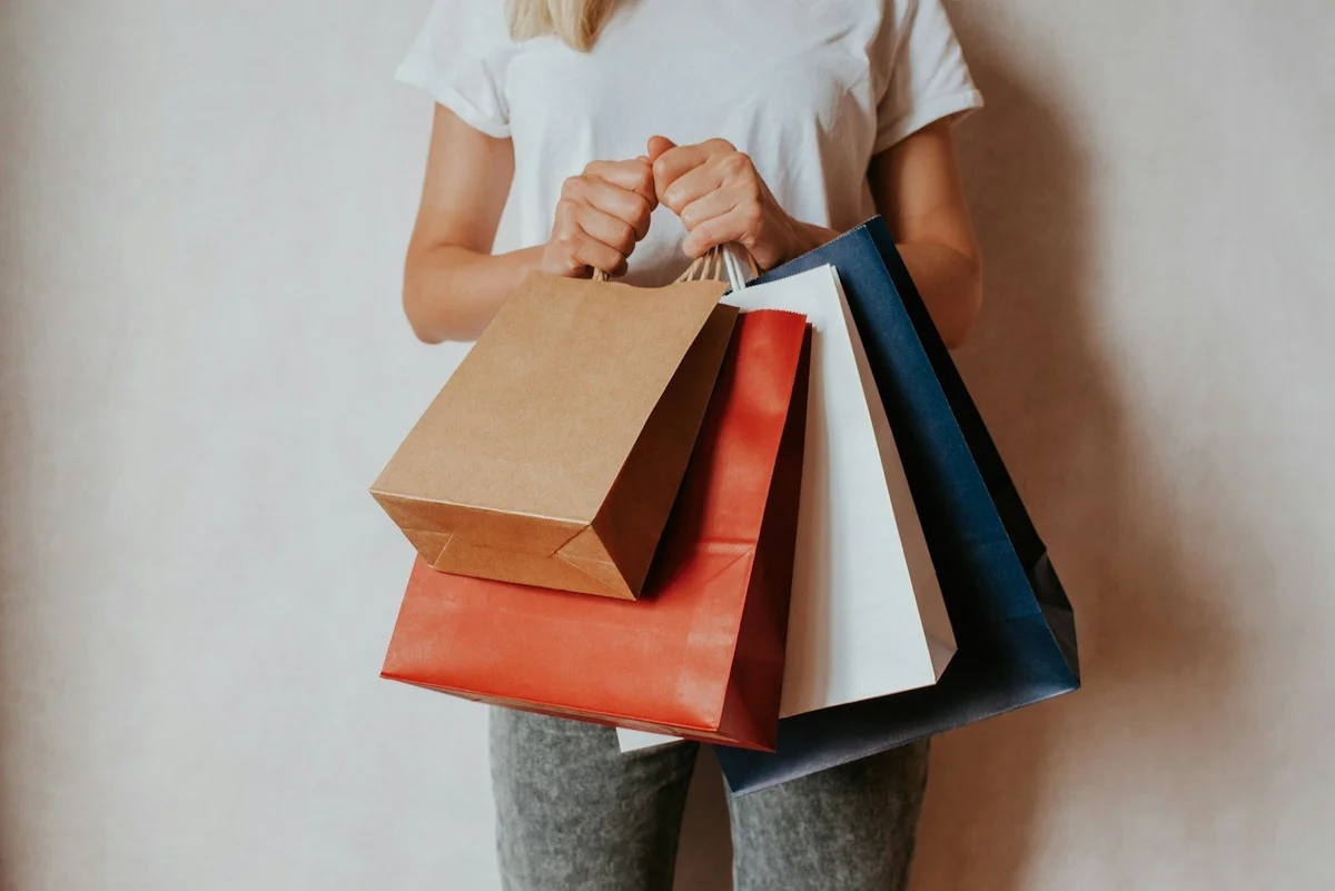 Person holding four shopping bags against a plain wall