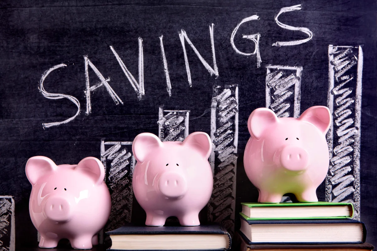 Three pink piggy banks on books beside a savings chart