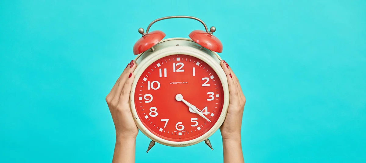 Hands holding a red alarm clock on turquoise background